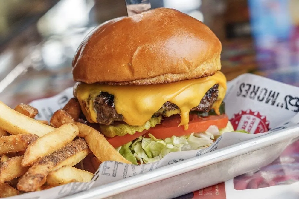 A cheeseburger with lettuce, tomato, pickles, and melted cheese served with fries on the side.